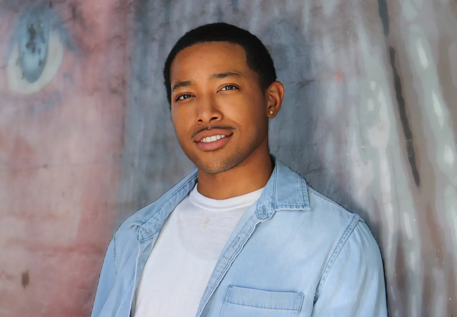 Malcolm Xavier smiling in a light denim shirt over a white T-shirt.